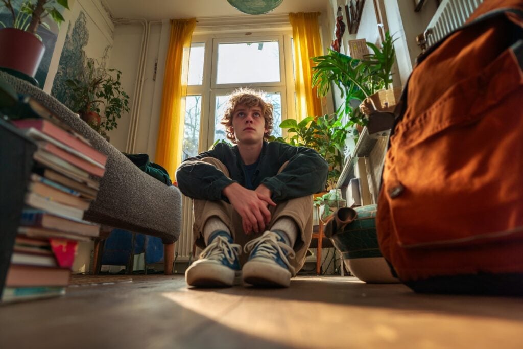 Jongen zit in slaapkamer onzeker, depressief, eenzaam op de grond